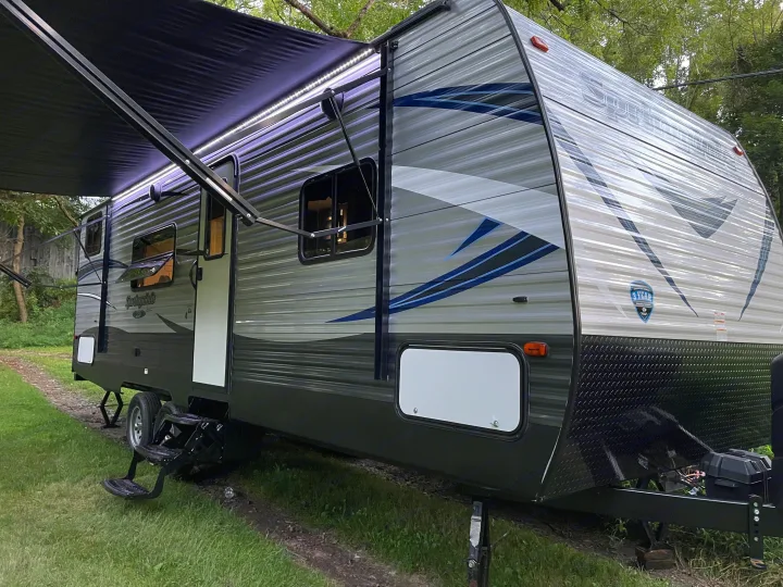 This Springdale RV rental is set up on grass with its awning extended and illuminated by LED lights. Ready for camping.. Keystone RV Springdale 2018