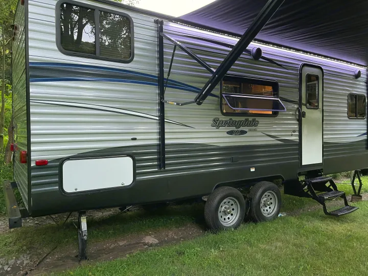 This Springdale RV rental is a striped gray travel trailer with an extended awning and LED lights, ready for camping.. Keystone RV Springdale 2018