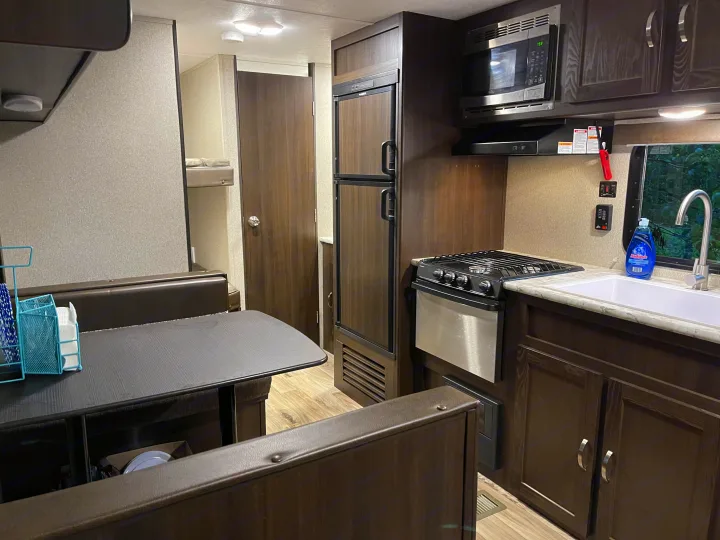 Inside a modern RV rental: a compact kitchen with stove, microwave, and sink, next to a dining booth and bunk beds.. Keystone RV Springdale 2018