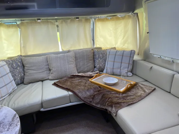 Spacious rv rental living area features a light U-shaped sofa with pillows, a soft throw, and a serving tray.. Airstream International 2014