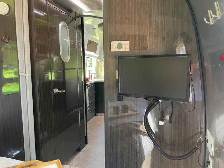 Modern rv rental interior showcasing a compact kitchen, TV, and Dometic thermostat on sleek dark wood-look walls.. Airstream International 2014
