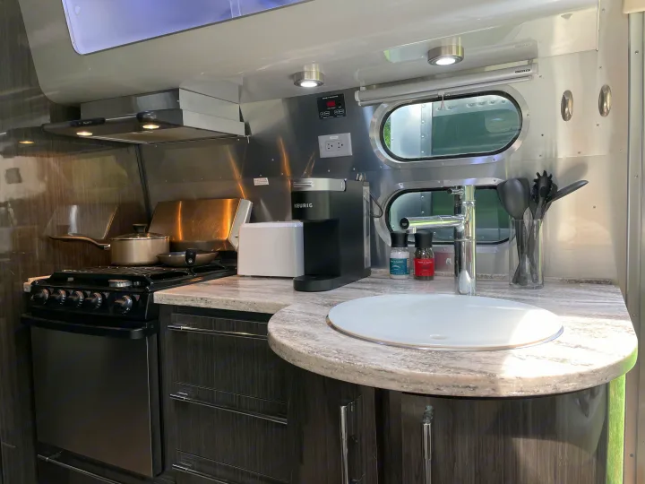 Modern RV rental kitchen featuring a stove, oven, sink, and coffee maker, perfect for compact travel cooking.. Airstream International 2014