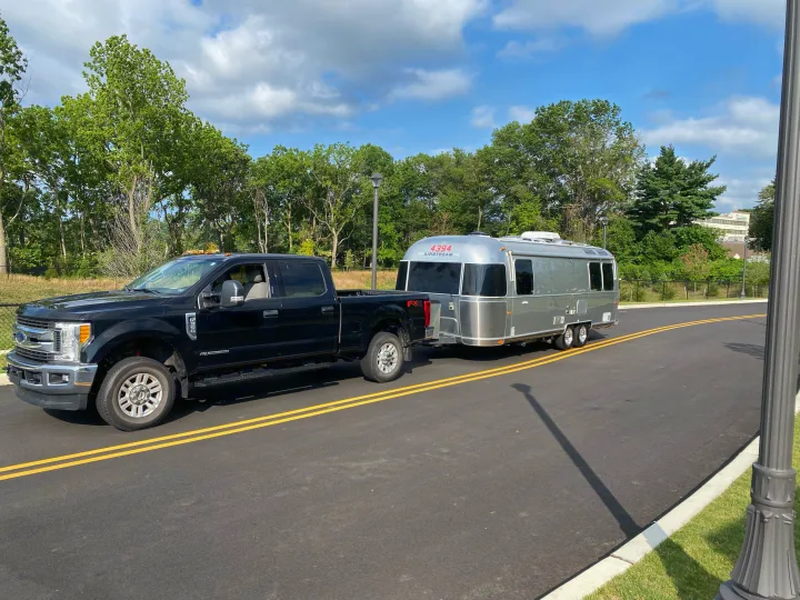 A black Ford pickup truck tows a silver Airstream RV rental down a paved road on a clear day.. Airstream International 2014