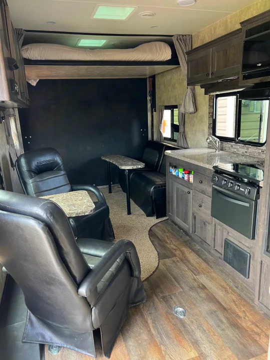 RV rental interior: a spacious living area with black leather recliners, a dinette, a kitchen with full amenities, and an elevated bunk bed.. Eclipse Recreational Vehicles Iconic 2018