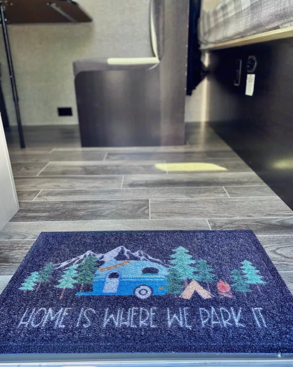 An RV doormat reads 'Home is where we park it' with an RV & camp scene, welcoming guests inside the spacious rv rental.. Jayco Jay Flight SLX 2022