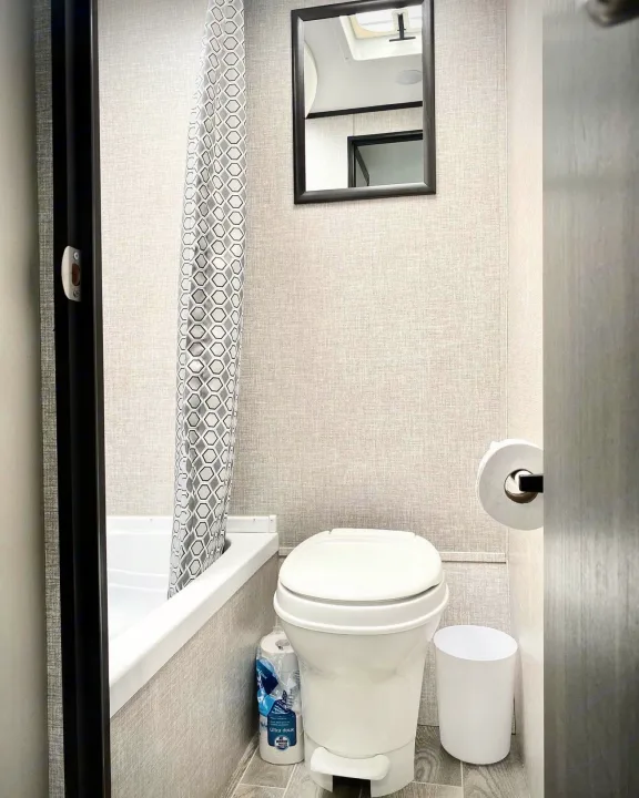 Inside an **rv rental**: a compact bathroom with a toilet, small tub/shower (geometric curtain), mirror, and toilet paper dispenser.. Jayco Jay Flight SLX 2022