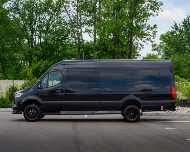 Sleek black Mercedes-Benz Sprinter van, perfect for RV rental, parked on asphalt with trees behind.. Midwest Automotive Designs Ultimate Coach 2023