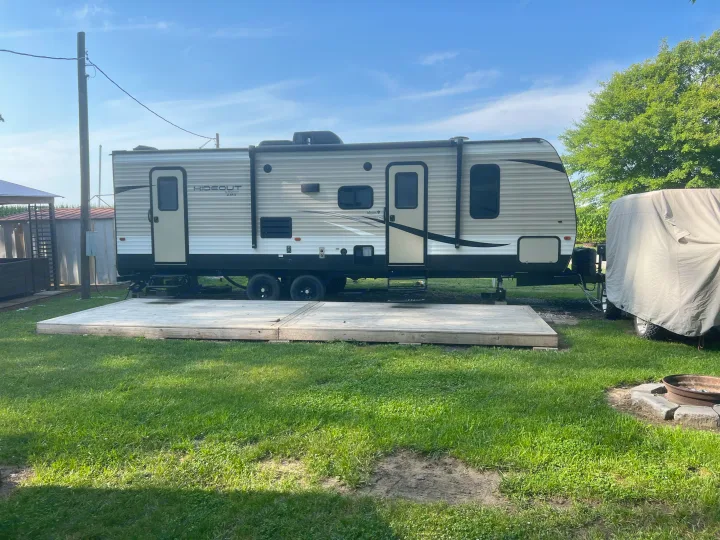 A large "Hideout" travel trailer RV is parked on a grassy site with a wooden deck, perfect for your RV rental adventure!. Keystone Hideout 2017
