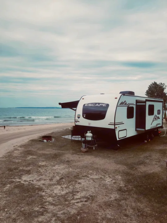 White Escape travel trailer rv rental parked beachfront. Ideal for scenic waterfront camping with a view of waves under a cloudy sky.. Escape e231bh 2022