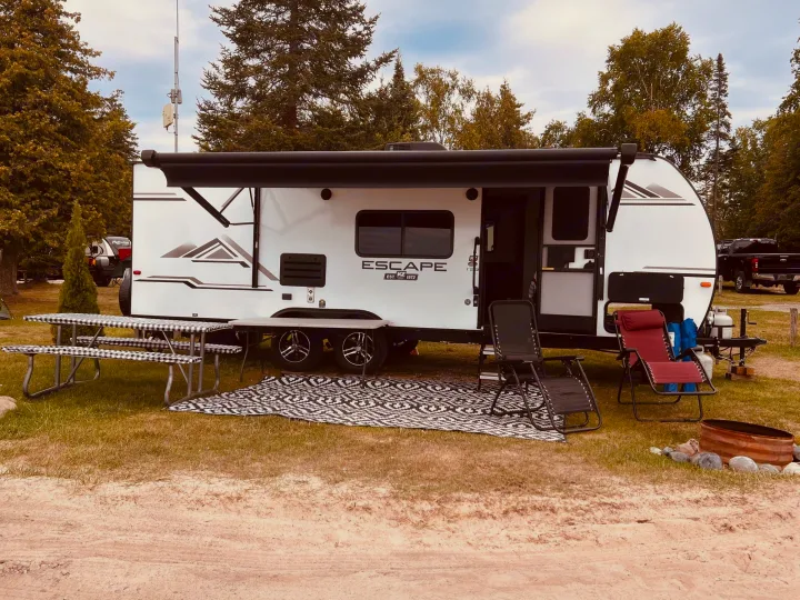 Enjoying an RV rental at a serene campsite with a picnic area, lounge chairs, and fire pit under an extended awning.. Escape e231bh 2022