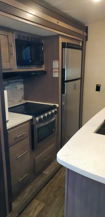 RV rental interior features a compact kitchen: microwave, stove, stainless steel fridge, and light counters.. Keystone Sunset Trail 2022
