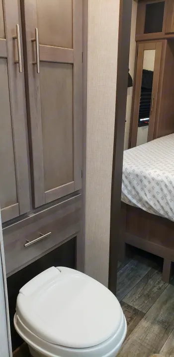 Compact RV rental interior: view of a bathroom with toilet & built-in cabinets, with the bedroom visible beyond.. Keystone Sunset Trail 2022