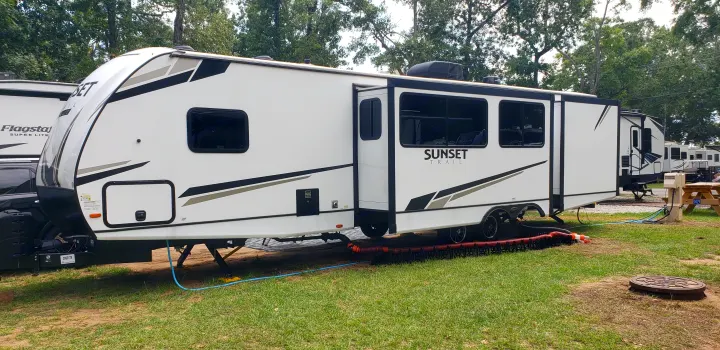 White Sunset Trail RV rental set up at a grassy campground site with utilities connected for a relaxing vacation.. Keystone Sunset Trail 2022