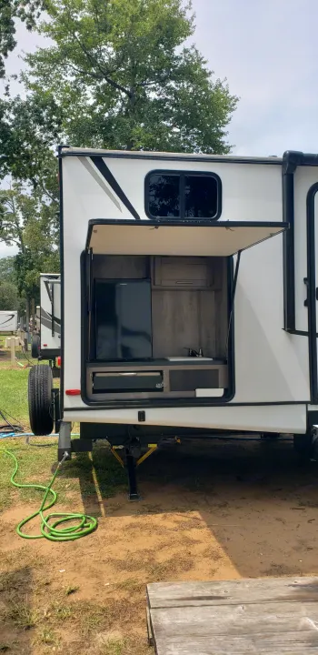 RV rental with an open outdoor kitchen: fridge, sink, and grill. Parked at a sunny campsite.. Keystone Sunset Trail 2022