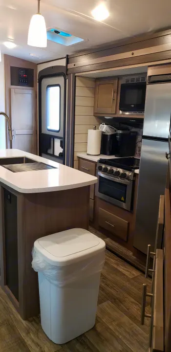 RV rental kitchen with island, sink, microwave, oven, fridge, and trash can on wood floor.. Keystone Sunset Trail 2022