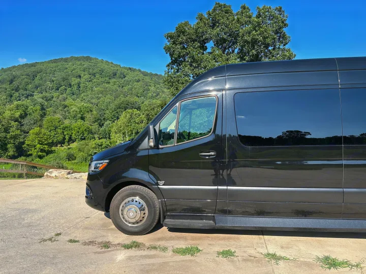 Black custom van, perfect for an RV rental adventure, parked before a scenic green mountain under a clear blue sky.. Ultimate Toys Ultimate Coach 2024