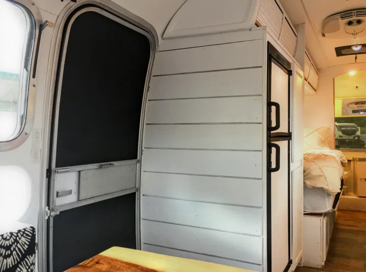 Inside an RV rental: features a screen door, white shiplap wall, refrigerator, and a glimpse of the bedroom.. Airstream Trade Wind 1976