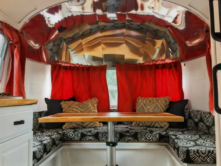 Inside an RV rental: Dinette with bold red curtains, black & white cushions, and reflective walls.. Airstream Trade Wind 1976