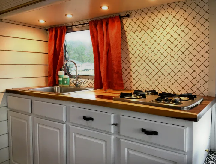 Stylish RV rental kitchenette with wood countertops, a sink, and stovetop, against a patterned backsplash.. Airstream Trade Wind 1976