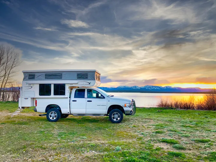 Scenic RV rental: White pop-up truck camper by a lake at sunset, with snow-capped mountains in the background.. Hallmark Everest 2011