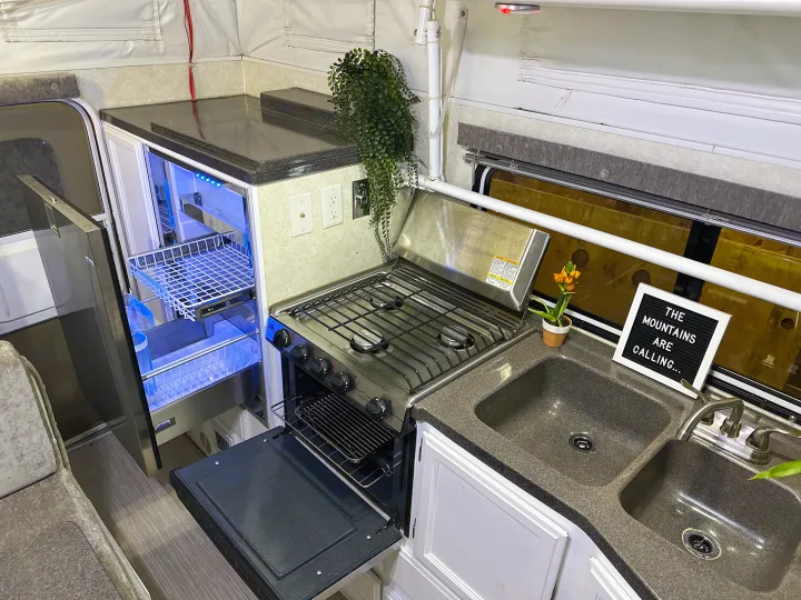 Cozy rv rental kitchen: a compact space with a fridge with blue lights, stove, oven, double sink, and mountain quote sign.. Hallmark Everest 2011