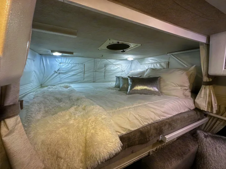 Cozy RV rental bed area featuring white linens, a fluffy throw, and modern interior details.. Hallmark Everest 2011