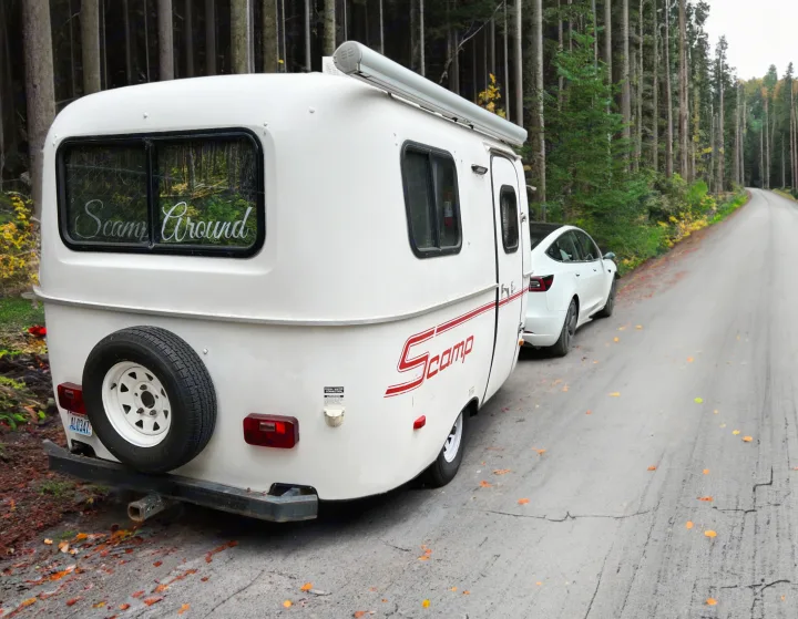 White Scamp travel trailer, ideal for RV rental, with a Tesla parked on a scenic forest road. "Scamp Around" on RV window.. Scamp Scamp Trailer 2007