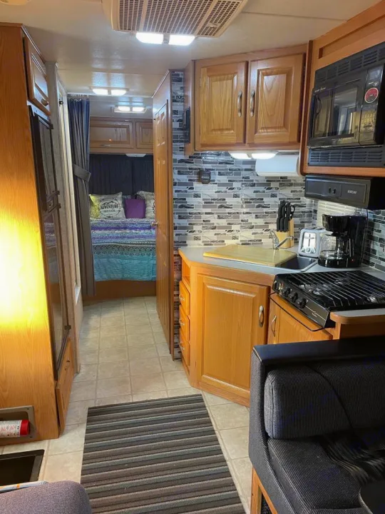Spacious RV rental interior with full kitchen, cozy bedroom area & wood accents. Perfect for road trip adventures.. Four Winds Majestic 2006