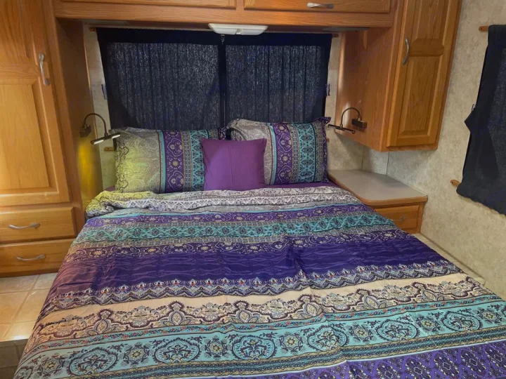 Inviting RV rental bedroom: vibrant patterned bedding, wooden cabinets, and wall-mounted reading lamps. Ready for adventure.. Four Winds Majestic 2006
