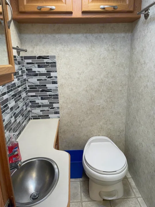 This RV rental bathroom features a clean toilet, stainless steel sink, and modern gray mosaic tile backsplash. Compact and functional.. Four Winds Majestic 2006