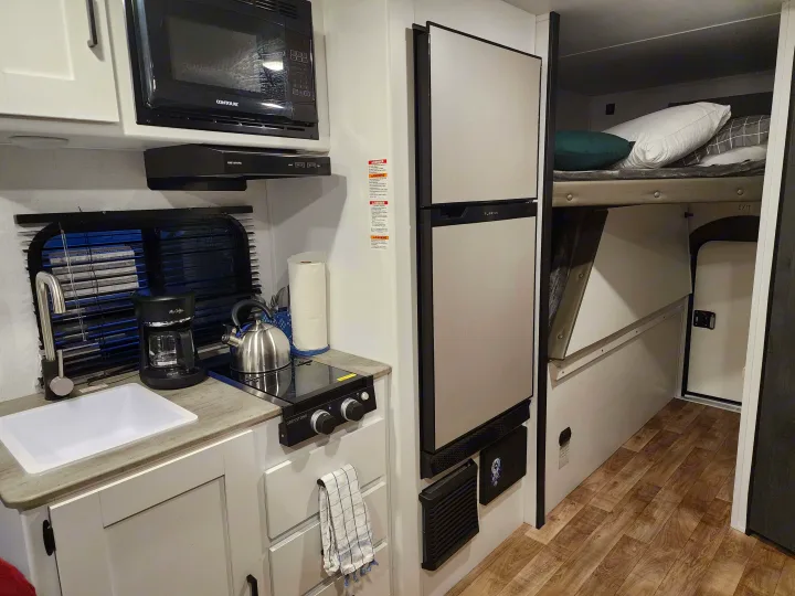 Tour this RV rental's cozy interior: a compact kitchen with microwave, fridge, stovetop, sink, and comfy bunk beds.. Keystone RV Hideout 2023