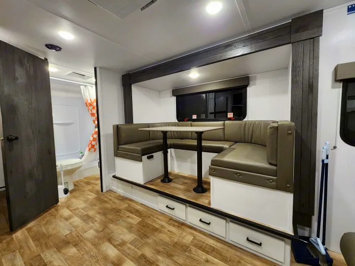 Spacious RV rental interior featuring a comfy dinette with storage drawers, modern wood-look flooring, and a private bathroom.. Keystone RV Hideout 2023