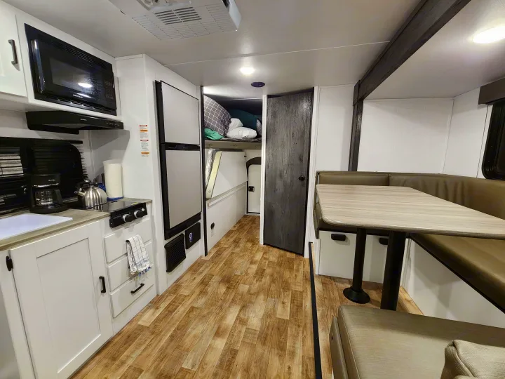 RV rental interior: Kitchen, large fridge, bunk beds, and dinette area with table and seating for compact living.. Keystone RV Hideout 2023