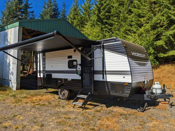 This rv rental, a Keystone Hideout travel trailer, with its awning extended, parked by a barn for camping.. Keystone RV Hideout 2023