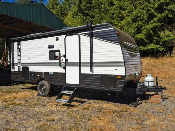 This Keystone Hideout travel trailer, a great option for an rv rental, is parked in a dry area with trees behind it.. Keystone RV Hideout 2023