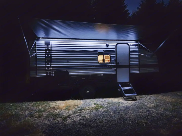 An RV rental, a sleek travel trailer, illuminated at night with its awning extended and steps down, ready for camp.. Keystone RV Hideout 2023