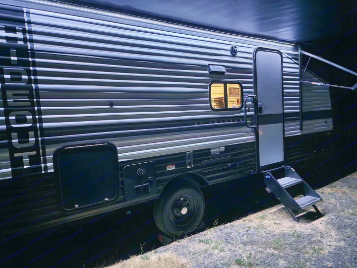 Night view of a dark rv rental, illuminated by interior and awning lights. The door is open with steps extended, ready for adventure.. Keystone RV Hideout 2023