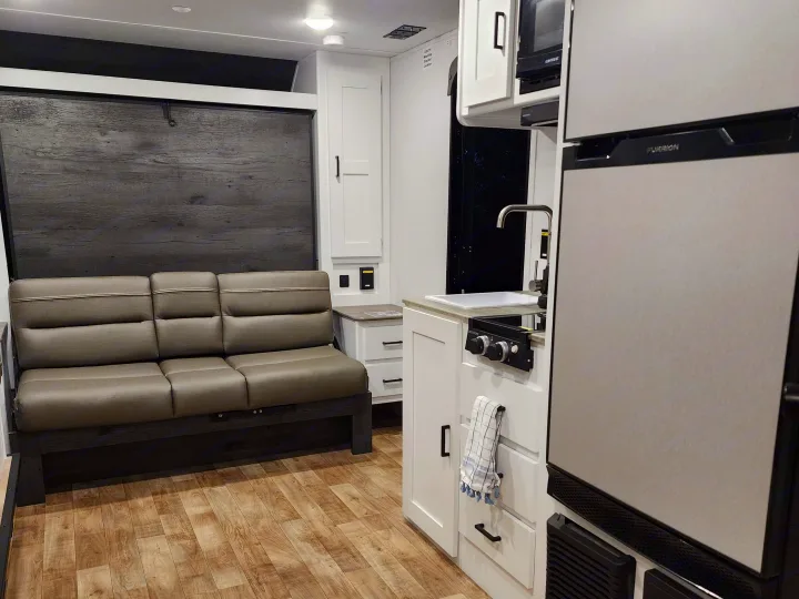 RV rental interior: A modern compact kitchen with appliances next to a comfortable grey sofa, all within a well-designed RV.. Keystone RV Hideout 2023