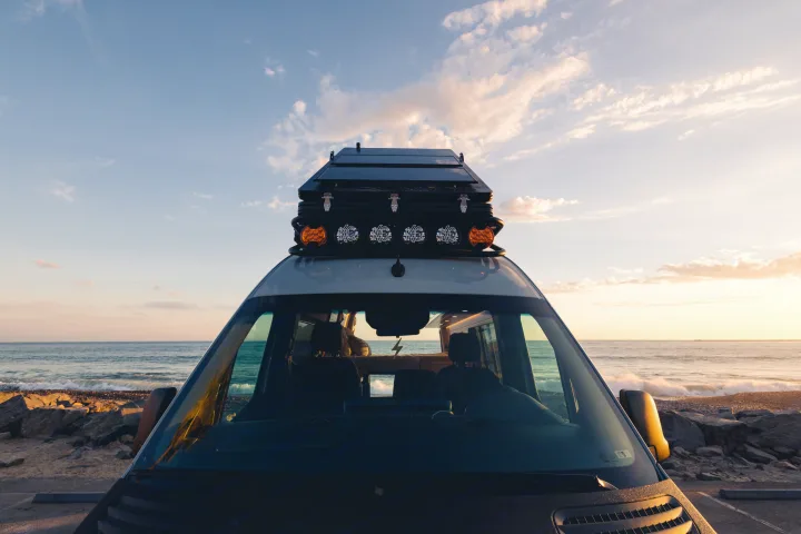 RV rental adventure: Camper van with rooftop tent parked beachfront at sunset for breathtaking ocean views.. Mercedes-Benz Sprinter 2023