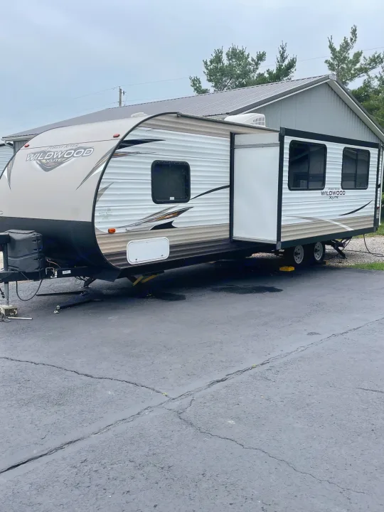 This RV rental is a Forest River Wildwood travel trailer, parked & leveled on asphalt with its slide-out extended.. Forest River Wildwood X-Lite 2019