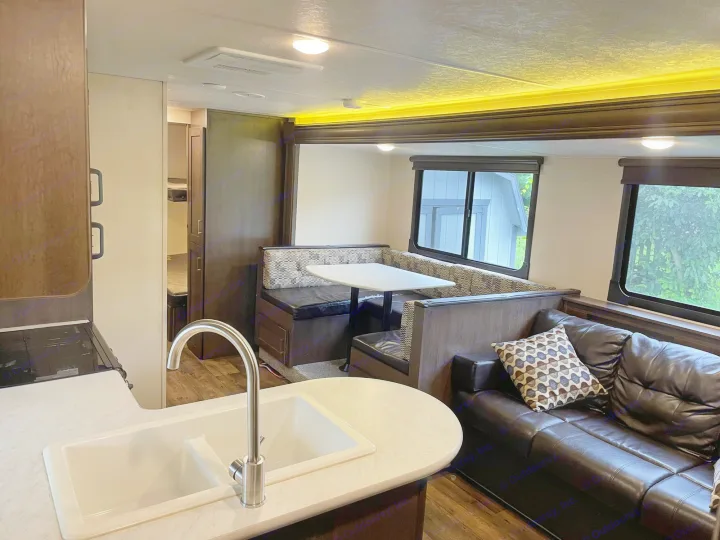 Experience this rv rental's inviting interior: modern kitchen with sink, spacious U-shaped dinette, and cozy sofa.. Forest River Wildwood X-Lite 2019