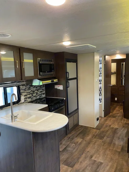 Inside this RV rental: a modern kitchen with dark cabinets, white counters, and wood-look floors. Ready for travel.. Forest River Wildwood X-Lite 2019