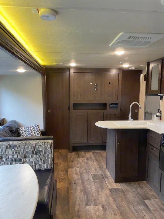 Inside a clean RV rental: modern kitchen, dinette, and living area with wood-look flooring and dark cabinetry.. Forest River Wildwood X-Lite 2019
