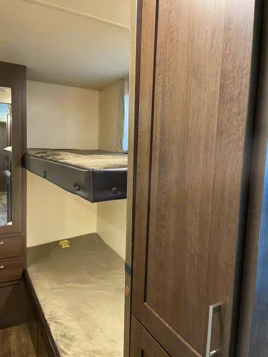 RV rental interior: two compact bunk beds with simple mattresses. Dark wood cabinetry and a mirrored wardrobe are visible.. Forest River Wildwood X-Lite 2019
