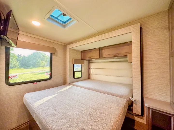 Explore a comfortable RV rental bedroom. It features a versatile bed, wall-mounted TV, skylight, and large window view.. Winnebago Minnie Winnie 2021