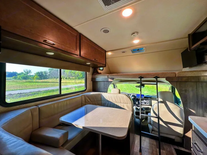 Inside a bright **rv rental**: dinette, overhead bunk with ladder, kitchen, and large windows with scenic outdoor views.. Winnebago Minnie Winnie 2021