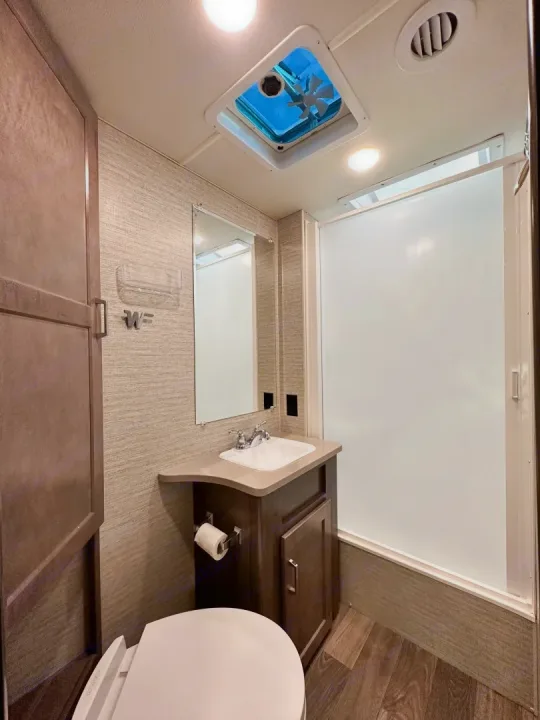 This functional RV rental bathroom features a compact toilet, vanity with sink, mirror, and enclosed shower.. Winnebago Minnie Winnie 2021