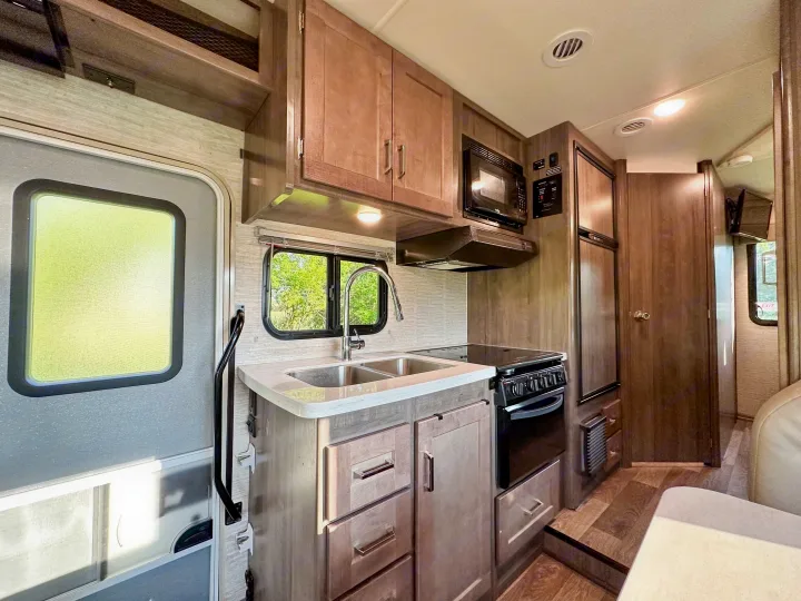 RV rental kitchen view: a fully equipped compact space with sink, stove, microwave, and fridge.. Winnebago Minnie Winnie 2021