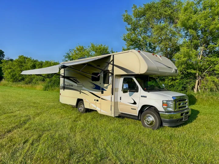 This beige Winnebago Minnie Winnie Class C RV rental, with its awning out, is ready for adventure in a grassy field.. Winnebago Minnie Winnie 2021