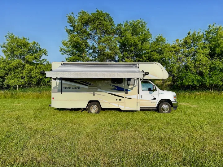Spacious Minnie Winnie RV rental parked in a sunny green field with trees. Perfect for outdoor travel & camping.. Winnebago Minnie Winnie 2021